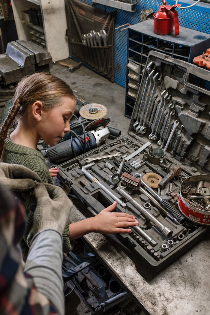 A girl examines tools in a mechanics workshop, showcasing curiosity and learning about auto repair.